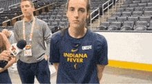 a man wearing an indiana fever shirt is standing in front of a microphone .
