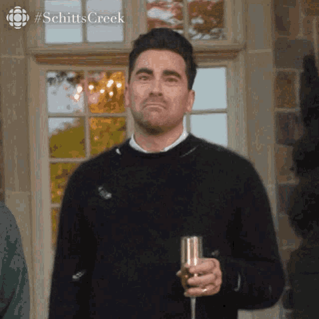 a man in a black sweater is holding a glass of champagne and making a funny face .