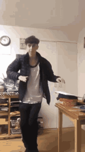 a man is dancing in a living room in front of a table and a clock .