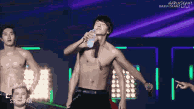 a man without a shirt is drinking water on stage