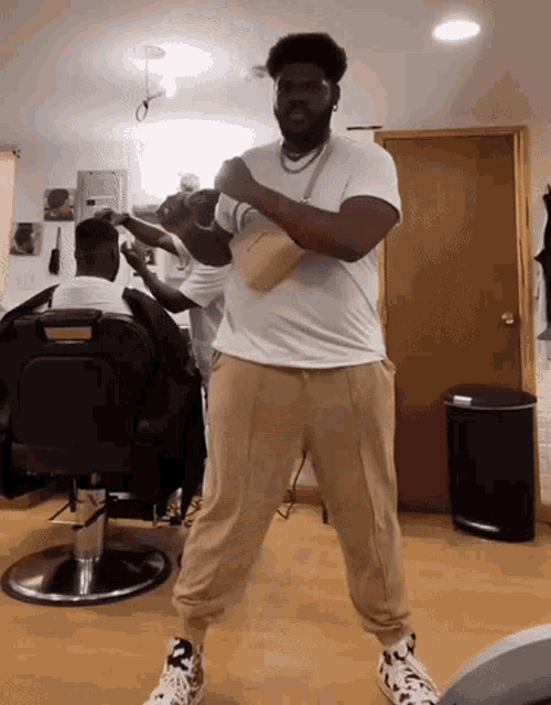 a man in a white shirt and tan pants is standing in front of a barber chair