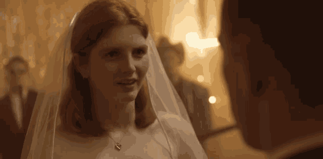 a woman in a wedding dress and veil looks at a man in a suit