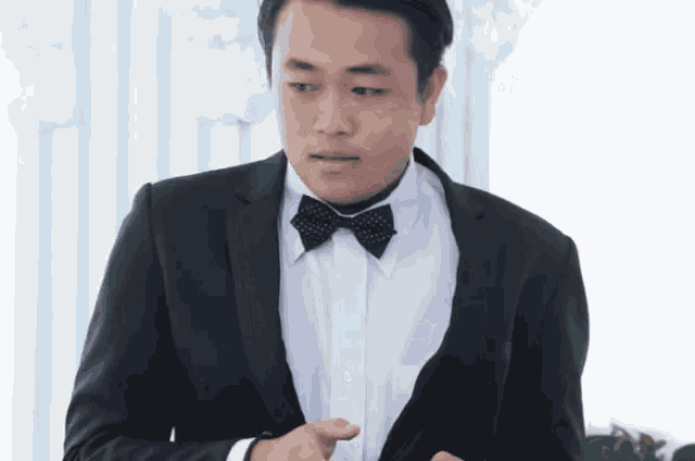 a man in a black suit and bow tie adjusts his jacket