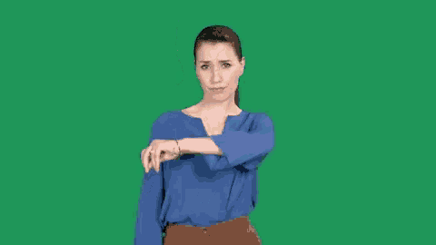 a woman in a blue shirt and brown pants is making a funny face and pointing at the camera .