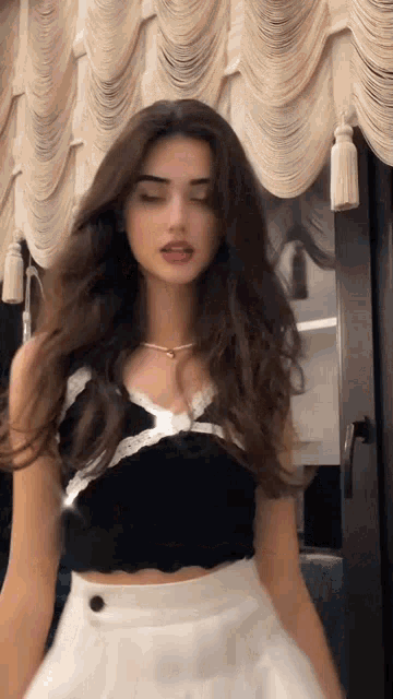 a woman in a black crop top and white skirt is standing in front of a curtain .