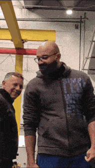 a man wearing a simple life sweatshirt stands next to a man wearing a mask