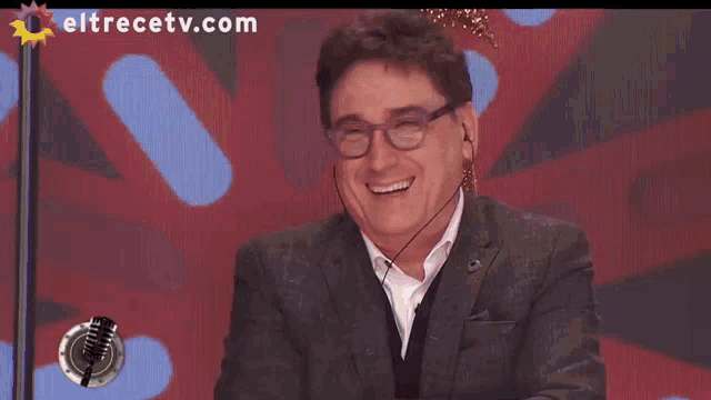 a man wearing glasses and earbuds is smiling in front of a screen that says eltrecetv.com