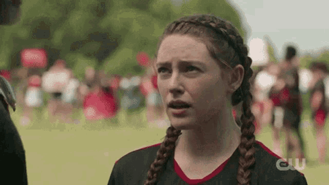 a girl with braids is standing on a field with a crowd of people in the background .