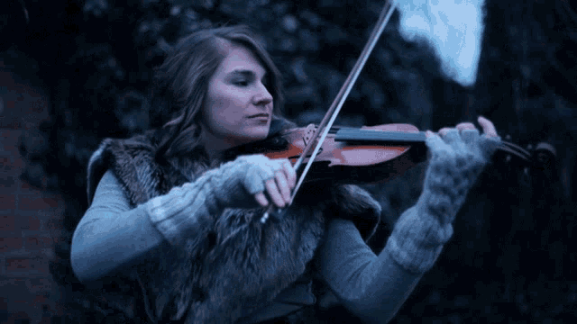 a woman in a fur vest is playing a violin in the dark