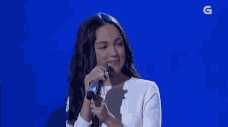 a woman in a white dress is singing into a microphone on a blue background .