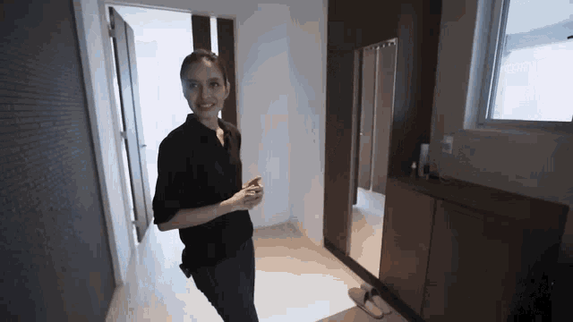 a woman in a black shirt is standing in a hallway in front of a mirror .