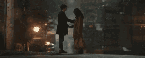 a man and a woman are standing on a sidewalk at night .