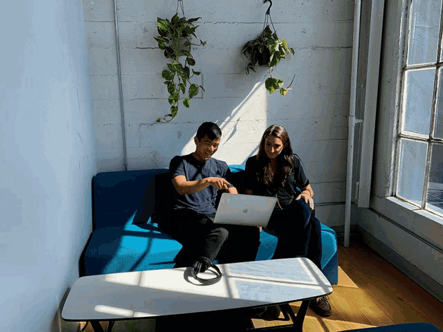 a man and a woman sit on a blue couch with a laptop