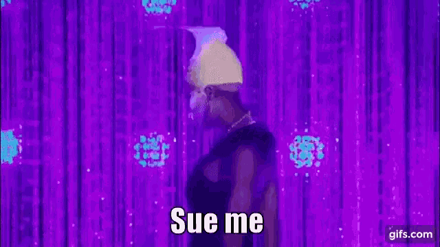 a drag queen is dancing on a stage in front of a purple curtain with the words `` sue me '' .