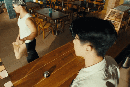a man in a white tank top is standing in a restaurant with tables and chairs