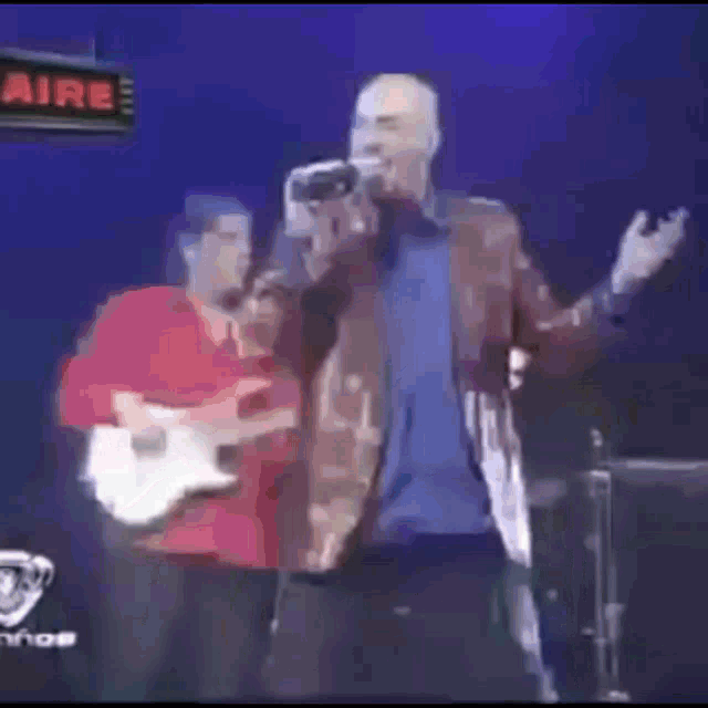 a man is singing into a microphone while another man plays a guitar on a stage .