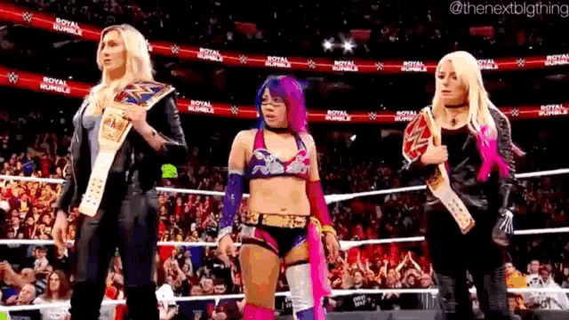 three women are standing next to each other in a wrestling ring holding belts .
