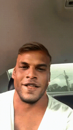 a man in a white shirt is making a funny face in a car