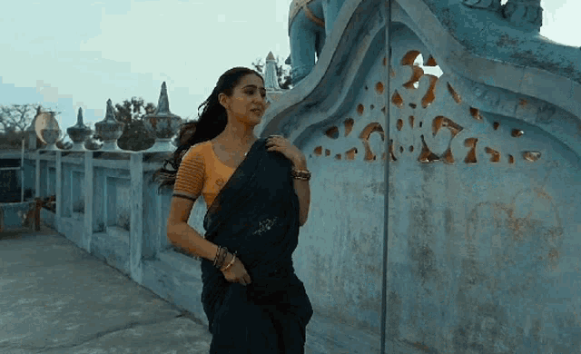 a woman in a black saree is standing next to a statue