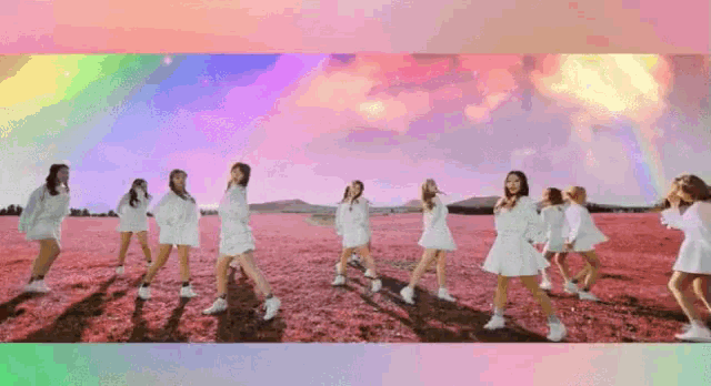 a group of girls in white dresses are dancing in a field with a rainbow in the background .