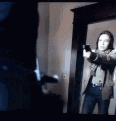 a woman is pointing a gun at a man in a room .