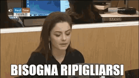 a woman is sitting at a desk in front of a computer with the words bisogna ripigliarsi written on it .