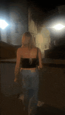 a woman in a black top and blue jeans is walking down a street