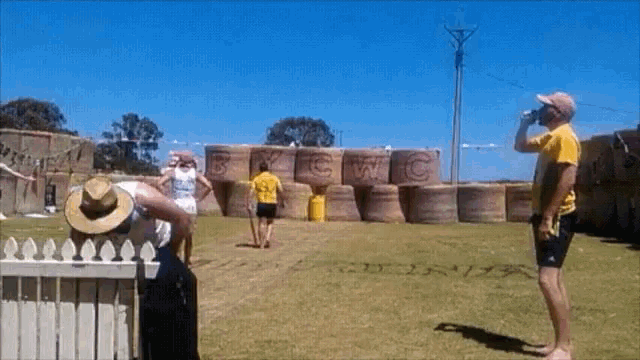 a man in a yellow shirt stands in front of a wall of hay bales with the letters cwc written on them