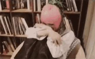 a woman in a pink hat is sitting in front of a bookshelf holding a black bag .