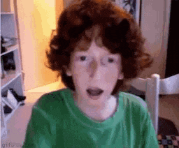 a young boy with red hair and a green shirt is making a funny face .