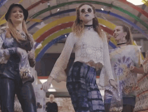 a woman wearing sunglasses and a choker stands in front of a rainbow archway