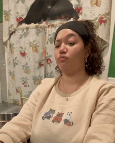 a woman wearing a sweater with cats and pumpkins on it makes a funny face