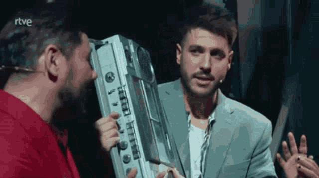 a man in a suit is holding a boombox and talking to another man