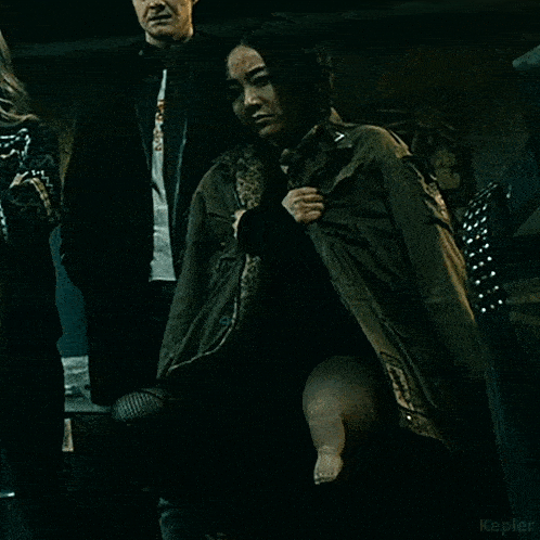a woman in a green jacket is holding a baby 's leg