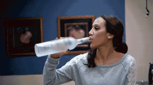 a woman is drinking from a bottle with the word vodka on the label