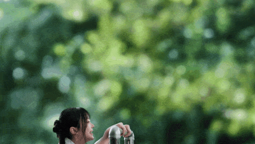 a woman is drinking water from a metal pipe