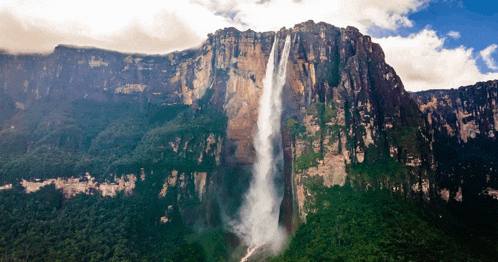 a waterfall in the middle of a mountain surrounded by trees and cliffs