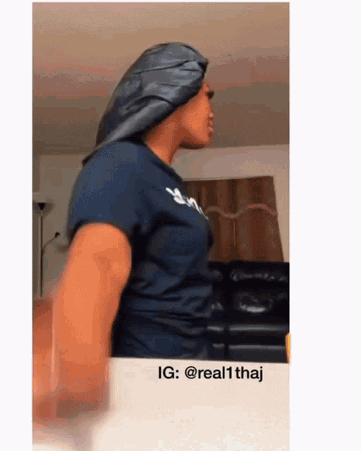 a woman in a blue shirt is standing in front of a couch with a caption that says ig : @ real1thai
