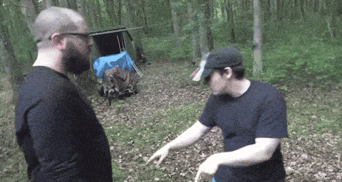two men are standing in the woods and one of them is pointing at something