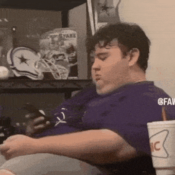 a fat man is sitting on a couch looking at his phone .