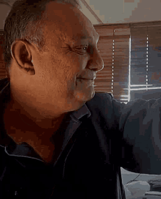 a man is smiling in front of a window with blinds on it .