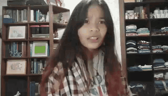 a girl in a plaid shirt is standing in front of a bookshelf filled with books