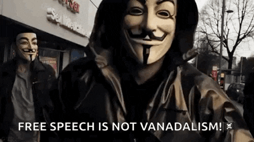 a man wearing a anonymous mask is standing in front of a building with the words `` free speech is not vanadaism '' .