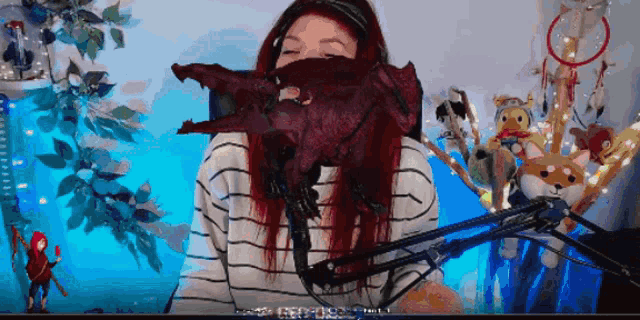a woman with red hair covering her face with a stuffed dragon