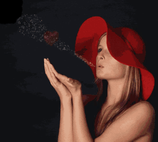 a woman wearing a red hat blows a heart out of her hands