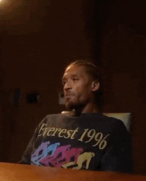 a man is sitting at a table wearing a black t-shirt that says `` everest 1996 '' .