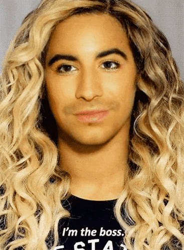 a man with blonde curly hair is wearing a black shirt that says i 'm the boss