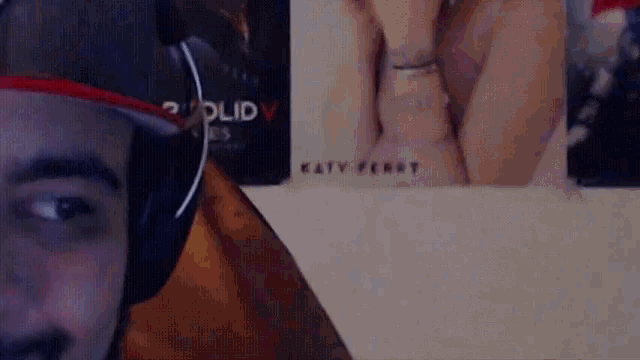 a man wearing headphones and a hat looks at a katy perry poster