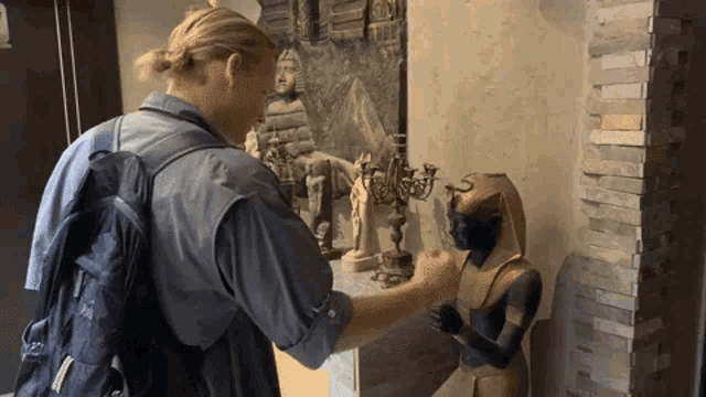 a man with a backpack is touching a statue of an egyptian king