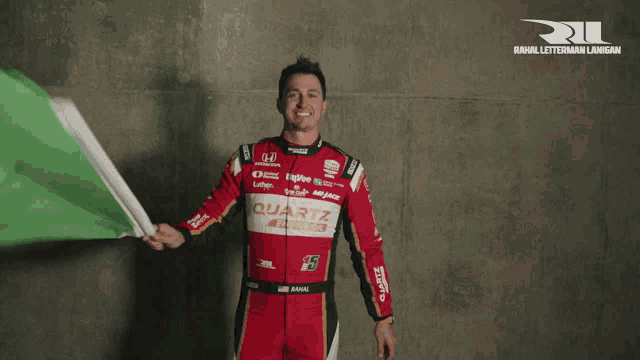 a race car driver holding a green flag with the word quartz on his shirt